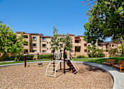 Thumbnail 19 of 21 - A playground with a slide and a swing set in front of apartment buildings. at The Maddox Sunnyvale Apartments, Sunnyvale, California