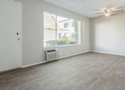 Thumbnail 23 of 39 - an empty living room with a large window and a ceiling fan at The Arches Apartments, California, 92021