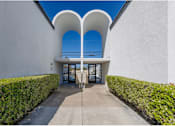 Thumbnail 5 of 39 - a walkway leading to the entrance of a white building with blue skiesat The Arches Apartments, LLC, El Cajon, CA