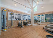 Thumbnail 20 of 24 - a gym with cardio machines and weights on a wooden floor at Napa Green Apartments LLC, Napa, CA 94559