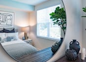 Thumbnail 72 of 78 - A bedroom with a round mirror and a bed with a grey blanket.