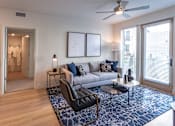 Thumbnail 65 of 78 - A living room with a grey couch, a black chair, and a blue patterned rug.