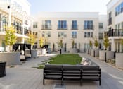 Thumbnail 46 of 78 - A black bench sits in the middle of a courtyard with apartment buildings in the background.