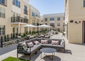Thumbnail 41 of 78 - A patio with a couch, chairs, and umbrellas is surrounded by apartment buildings.
