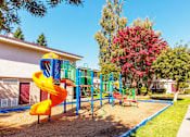 Thumbnail 8 of 11 - A playground with a yellow slide and a red bench.