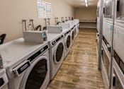 Thumbnail 8 of 9 - A row of front-loading washing machines are lined up in a laundromat.
