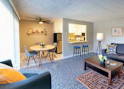 Thumbnail 3 of 9 - A living room with a grey couch, a coffee table, and a dining table with chairs.
