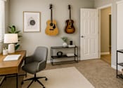 Thumbnail 7 of 12 - A room with a chair, a desk, and two guitars hanging on the wall.