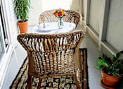 Thumbnail 4 of 9 - A balcony with a wicker chair and table with a potted plant on the side.