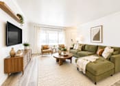 Thumbnail 1 of 11 - A living room with a green couch and a wooden cabinet.