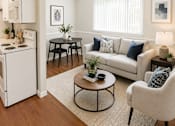 Thumbnail 2 of 8 - A living room with a white couch, a coffee table, and a kitchen area in the background.