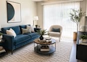 Thumbnail 3 of 14 - A living room with a blue couch, a white chair, and a coffee table with decorative items on it.