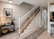 Thumbnail 3 of 11 - A well-lit foyer with a staircase, a bar stool, and a framed artwork on the wall.