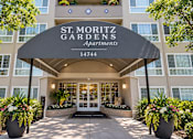 Thumbnail 12 of 13 - The front entrance of the St. Moritz Gardens Apartments is welcoming with a black awning and two large planters with flowers.