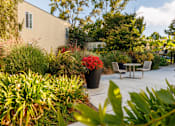 Thumbnail 6 of 8 - A patio with a table and chairs surrounded by green plants.