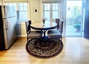 Thumbnail 2 of 10 - A dining room with a table and chairs and a refrigerator.