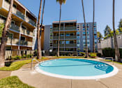Thumbnail 4 of 4 - A swimming pool in front of a multi-story apartment building with palm trees.