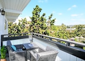 Thumbnail 4 of 10 - A balcony with a table and chairs overlooking a lush green landscape.