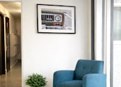 Thumbnail 10 of 14 - A blue chair sits in front of a framed picture of a car.