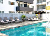 Thumbnail 8 of 14 - A pool with lounge chairs in front of a building.
