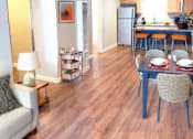 Thumbnail 3 of 8 - A living room with a couch, a table with chairs, and a kitchen area in the background.