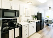 Thumbnail 2 of 13 - A black and white kitchen with a stove, microwave, and refrigerator.