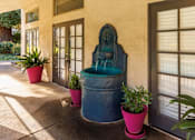 Thumbnail 8 of 8 - A blue fountain is in the middle of a concrete area with potted plants on each side.
