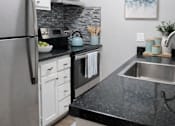 Thumbnail 2 of 12 - A modern kitchen with a black countertop and stainless steel appliances.