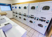 Thumbnail 11 of 13 - A row of washing machines are lined up in a laundromat.