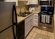 Thumbnail 4 of 9 - A kitchen with a black fridge, stove, and microwave.