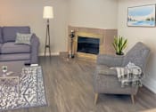 Thumbnail 4 of 8 - A living room with a grey couch, a grey armchair, a fireplace, and a painting on the wall.