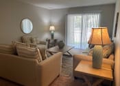 Thumbnail 8 of 8 - A living room with a tan couch, a wooden table, and a lamp.