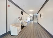 Thumbnail 5 of 11 - a long hallway with white walls and chairs and a staircase at The Franklin at Hillsborough Apartments, Des Moines