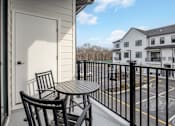 Thumbnail 11 of 63 - A balcony with a table and chairs overlooks a parking lot.