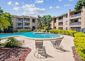 Thumbnail 1 of 7 - A pool surrounded by chairs and plants in front of apartment buildings.