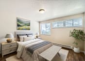 Thumbnail 18 of 28 - A bedroom with a large bed, a nightstand with a lamp, a painting on the wall, and a potted plant.