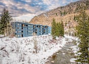 Thumbnail 26 of 28 - A blue building is situated by a stream in a snowy landscape.