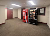 Thumbnail 2 of 6 - A Coca-Cola vending machine is in the middle of a carpeted room.