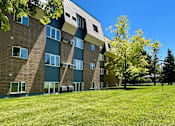 Thumbnail 21 of 24 - a brick apartment building with green grass and trees