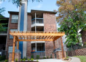 Thumbnail 5 of 30 - the view of a brick apartment building with a wooden porch at Infinity on the Mark, Dallas, TX, 75243