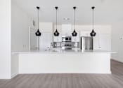 Thumbnail 3 of 17 - A modern kitchen with a white island and pendant lights.
