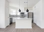 Thumbnail 4 of 17 - A modern kitchen with a white island and pendant lights.