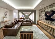 Thumbnail 21 of 24 - A modern living room with a brown leather couch and a large TV mounted on the wall.