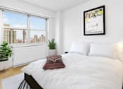 Thumbnail 9 of 12 - A bedroom with a large bed and a window overlooking a cityscape at The Caldwell Apartments, New York, 10028