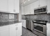 Thumbnail 11 of 12 - A kitchen with granite countertops and stainless steel appliances at The Caldwell Apartments, New York, NY, 10028