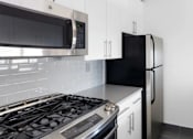 Thumbnail 2 of 17 - A black refrigerator sits in a kitchen with white cabinets at The Ellington Apartments, New York, 10019