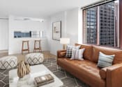 Thumbnail 1 of 17 - A living room with a brown leather couch, a white coffee table, and a large window overlooking the city at The Ellington Apartments, New York, NY