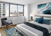Thumbnail 5 of 17 - A bedroom with a large bed, a chair, and a painting on the wall at The Ellington Apartments, New York, NY, 10019