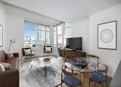 Thumbnail 5 of 15 - A living room with a brown couch, a glass table, and a television at The Maximilian Apartments, Long Island City, NY, 11101