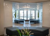 Thumbnail 14 of 22 - A spacious waiting area with a bench in the foreground and a view of a lounge area through the glass wall.